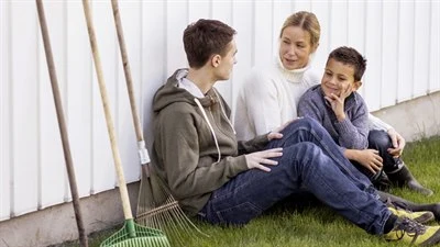 Blond kvinna i vit polotröja sitter med två pojkar. Båda har brunt hå, den ena har brun tröja och den andra har grå tröja. 