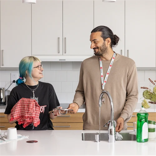 En man och en ung kvinna står i ett kök och diskar, de tittar på varandra, de är glada