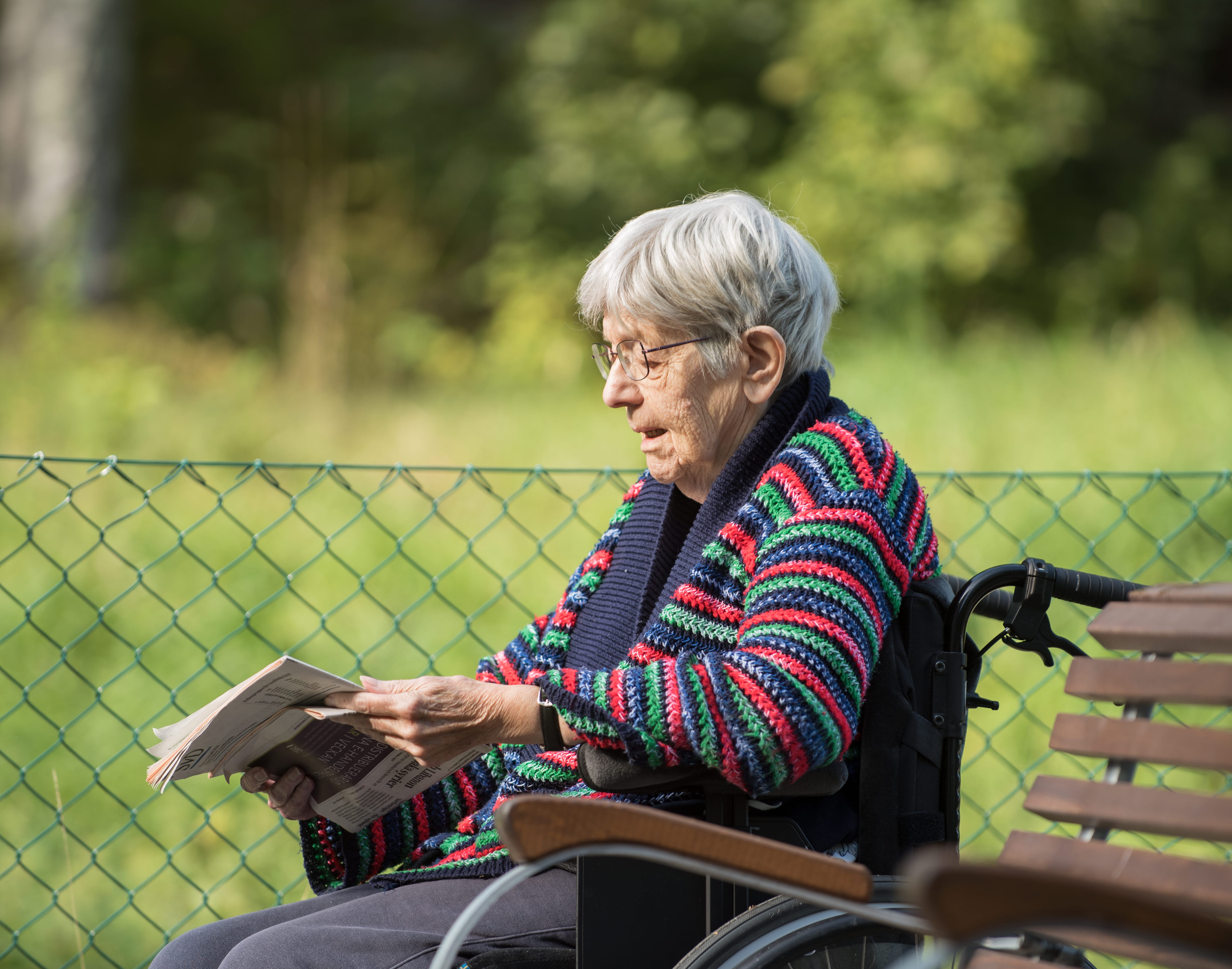 An elderly lady sits in her wheelchair and reads the newspaper