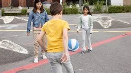 En kvinna, en flicka och en pojke, spelar fotboll på en asfaltsplan
