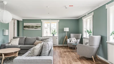 Vardagsrum med gröna väggar och trägolv. I rummet står till vänster en soffa i grått med ett soffbord i trä.