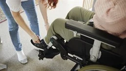 assistent hjälper en person i rullstol med skorna