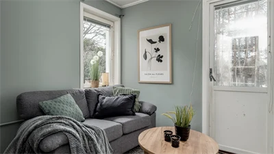 Grå soffa med runt träbord mot mintgrön vägg med ett fönster och en vit dörr