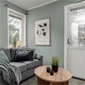 Grå soffa med runt träbord mot mintgrön vägg med ett fönster och en vit dörr