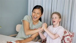 Kvinna och barn sitter vid bord, de skrattar och håller varandras händer
