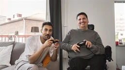 två män är glada och spelar tv spel en sitter i soffa och en i elrullstol
