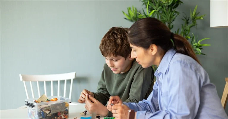 En kvinna och en pojke sitter vid ett bord och leker med lego