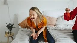 en kvinna sitter i sängen och skrattar
