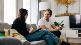 A girl and a boy are sitting on the couch with a tablet and a cell phone