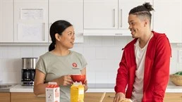 En kvinna med Humana tröja och en ung man står i ett kök, framför dem finns bröd juice och mjölk 