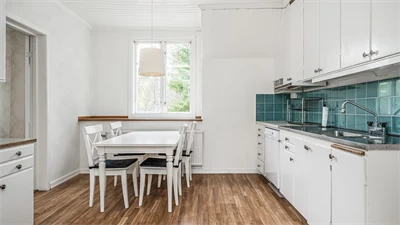 Kök i vitt med blått kakel. I rummet står ett matbord och stolar i vitt. 