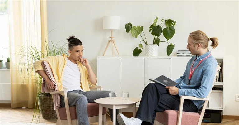En man och en ung man sitter i två fåtöljer och samtalar 
