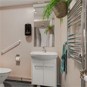 Toalett med beige duschdrapperi och grön palm som hänger på väggen. 