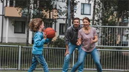 Three people playing basketball on artificial grass.