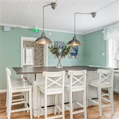 Kök med gröna väggar och trägolv. I rummet står ett matbord med träskiva och stolar i vitt. 
