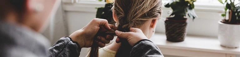 An adult braids a girl's hair.