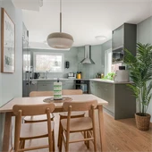 Kök med ljusgröna väggar, matbord i trä och en palm till höger.