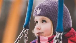 A girl is standing under a swing.