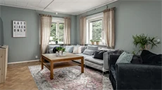 Vardagsrum en ljusgrå soffa och en svart fåtölj mot en mintgrön vägg med två fönster