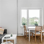 Rum med soffa och matbord, trägolv och vita väggar