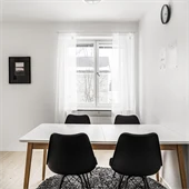 Vitt och brunt matbord framför ett fönster med vita gardiner 