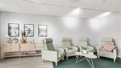 Loungeområde med stolar i ljusgrönt och soffbord i vitt. Står på en mörkgrön matta. 