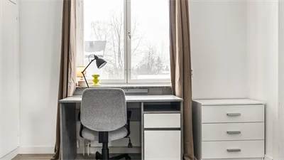 Skrivbord och stol framför ett fönster med beige gardin 