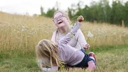 Två glada flickor leker i gräset vid ängen, det är sommar
