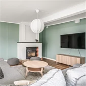 Vardagsrum med gröna väggar och trägolv. I rummet står till vänster en soffa i grått med ett soffbord i trä.