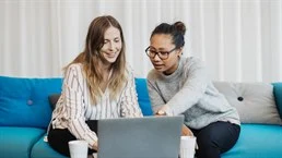 två kvinnor i en soffa som diskuterar vad som händer på datorn