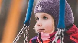 A girl is standing under a swing.