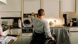 en man i rullstol öppnar ett skåp i köket