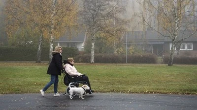 En person kör en kvinna med permobil. Hund går brevid.