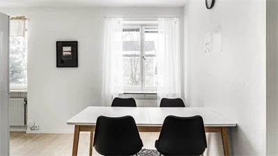 Vitt och brunt matbord framför ett fönster med vita gardiner 