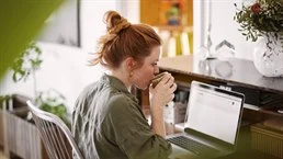 Kvinna som dricker kaffe och tittar på sin dator