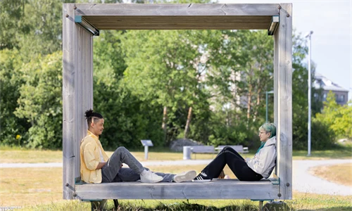 En ung man och en ung kvinna sitter i en träbox utomhus, de sitter mittemot varandra