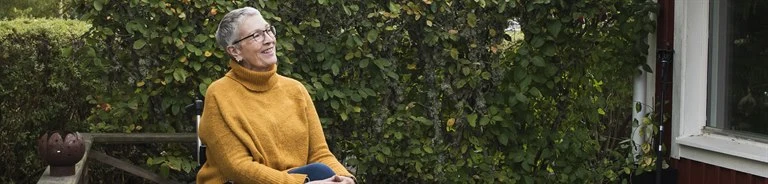 Kvinna sitter leende i permobil på altanen
