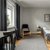Sovrum med grå matta grå säng mot vit vägg, fönster och skrivbord