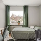 Sovrum med skrivbord till vänster och säng med grönt överkast och gröna gardiner. 
