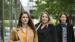 Tre kvinnor i ytterkläder står på trottoar